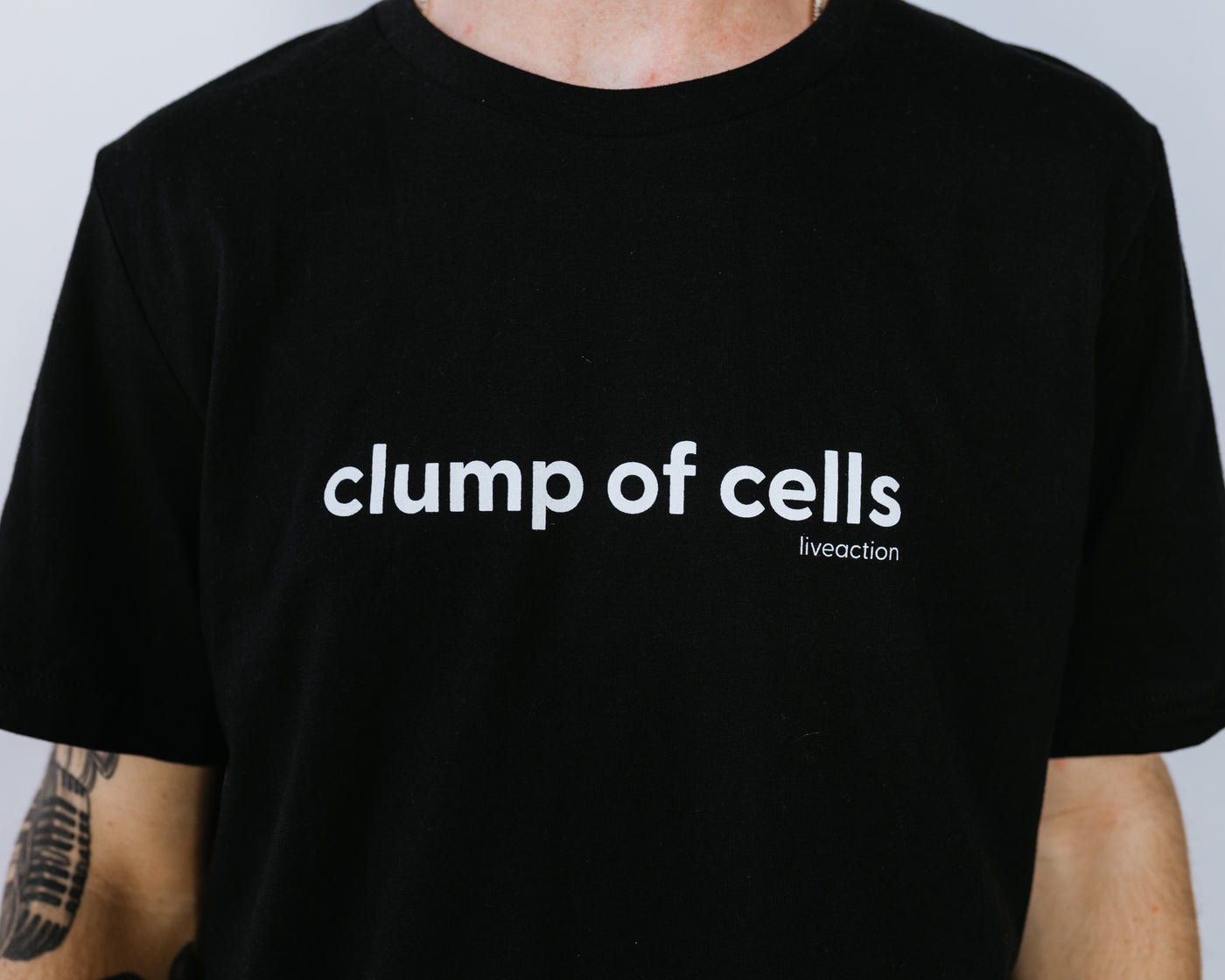 Close up of a man with dark brown hair and light beard in a black tee that says "clump of cells" across the chest in all lowercase. The Live Action brand is underneath the word "cells" in small font aligned to the right.