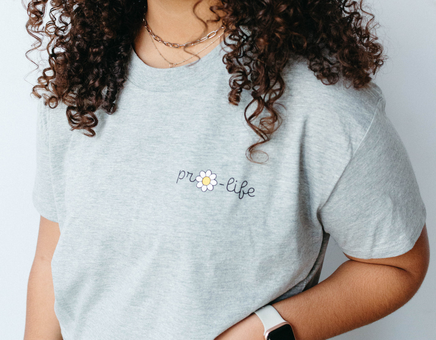 A heather gray crop tee with pro-life written near the top right shoulder with a daisy replacing the o in pro.