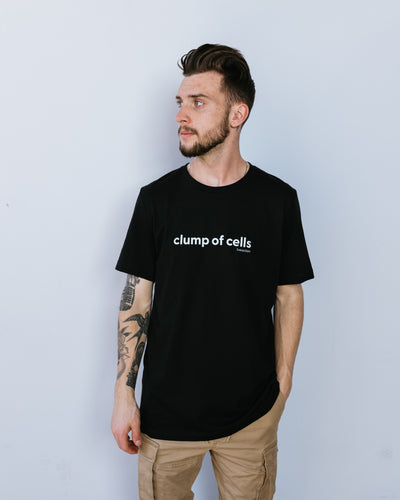 A man with dark brown hair and light beard in a black tee that says "clump of cells" across the chest in all lowercase. The Live Action brand is underneath the word "cells" in small font aligned to the right.