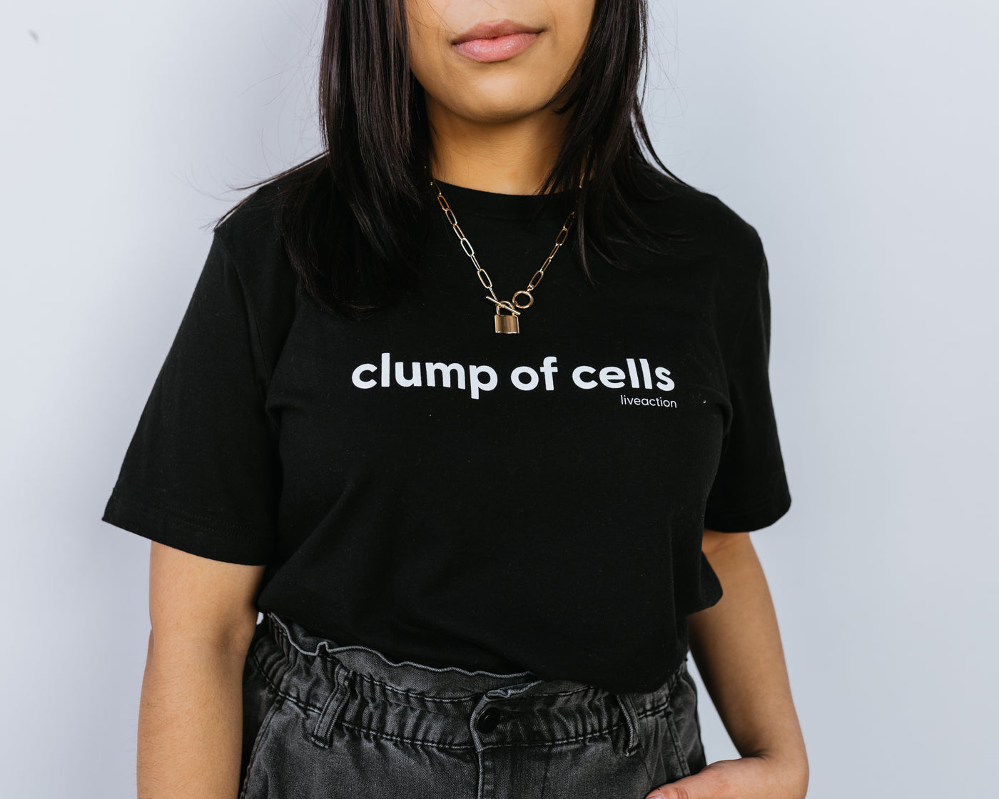 Closeup of a woman with black hair in a black tee that says "clump of cells" across the chest in all lowercase. The Live Action brand is underneath the word "cells" in small font aligned to the right.